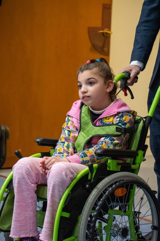 A young girl in a green wheelchair, pushed by a supporter at an Alliance event